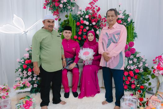 Engagement ceremony with vibrant floral backdrop, featuring a couple and family, dressed in traditional attire.