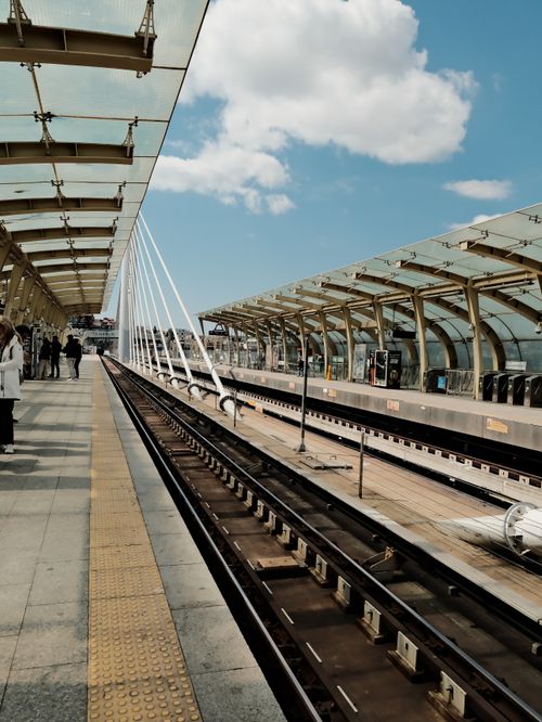 Free Sleek train station platform under clear blue sky with scattered clouds, featuring striking modern architecture. Stock Photo