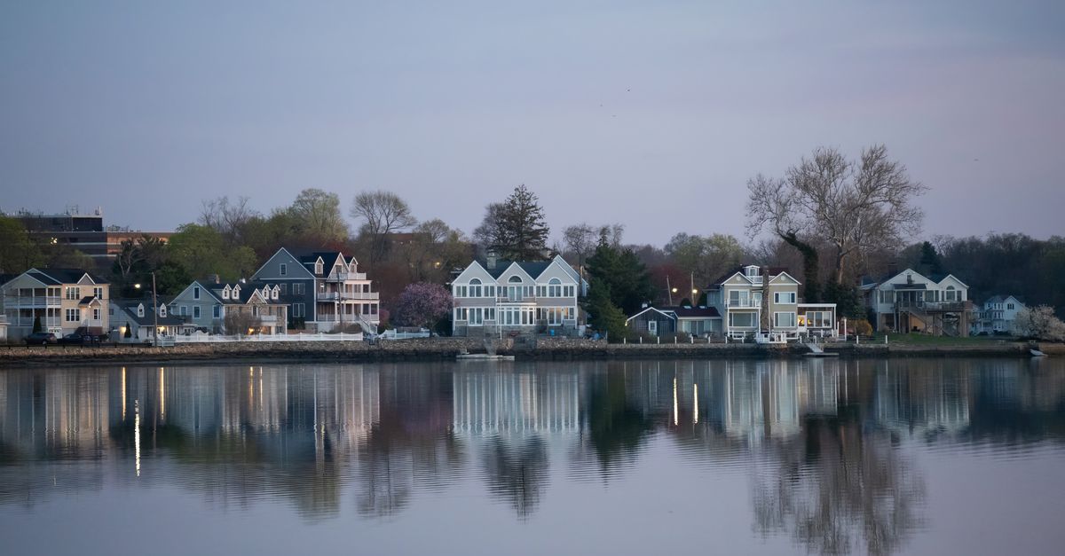 Peaceful lakeside view with houses reflected on the water during twilight.