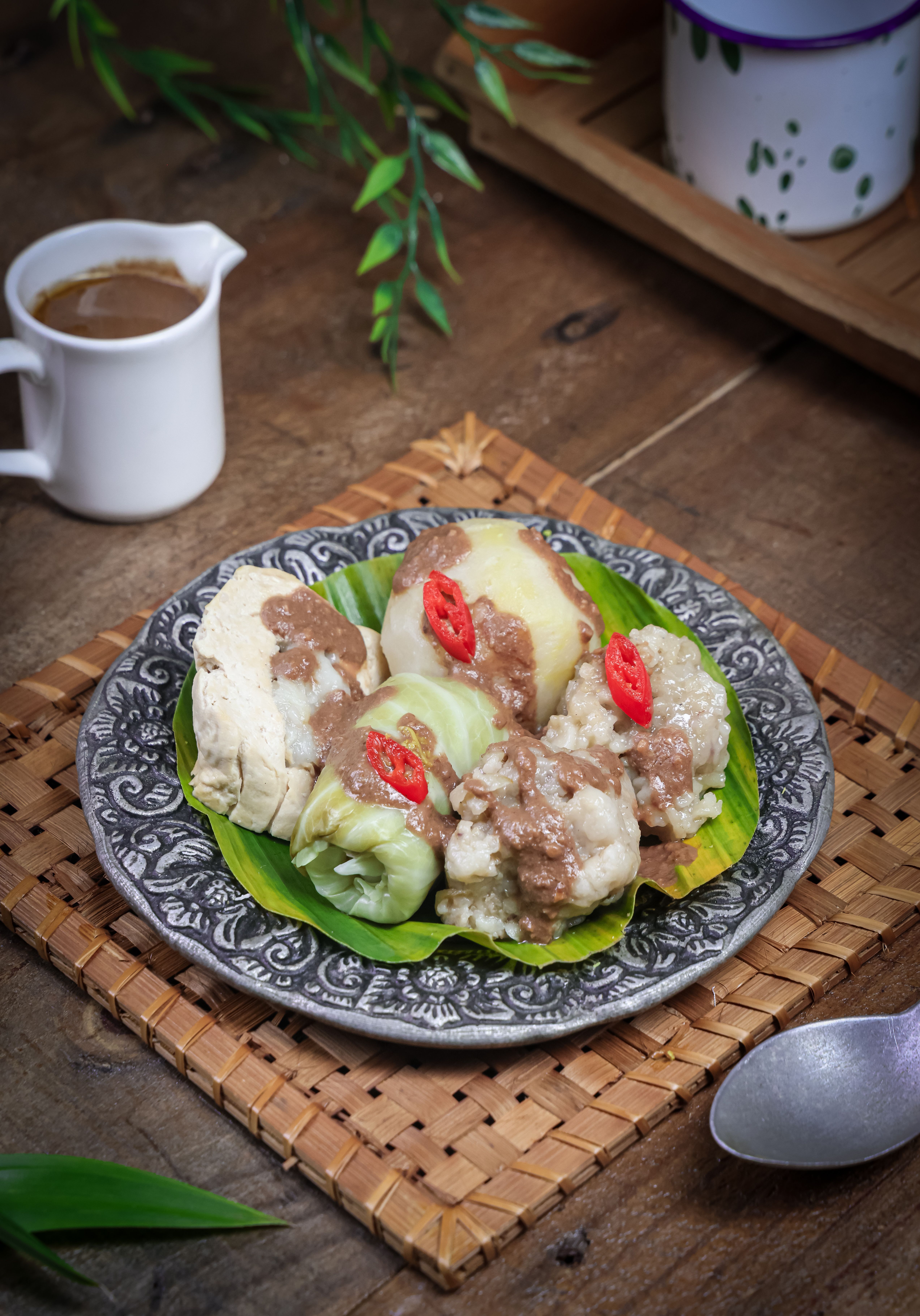 Delicious Indonesian gado-gado salad with peanut sauce, vegetables, and tofu on a rustic wooden table setting.