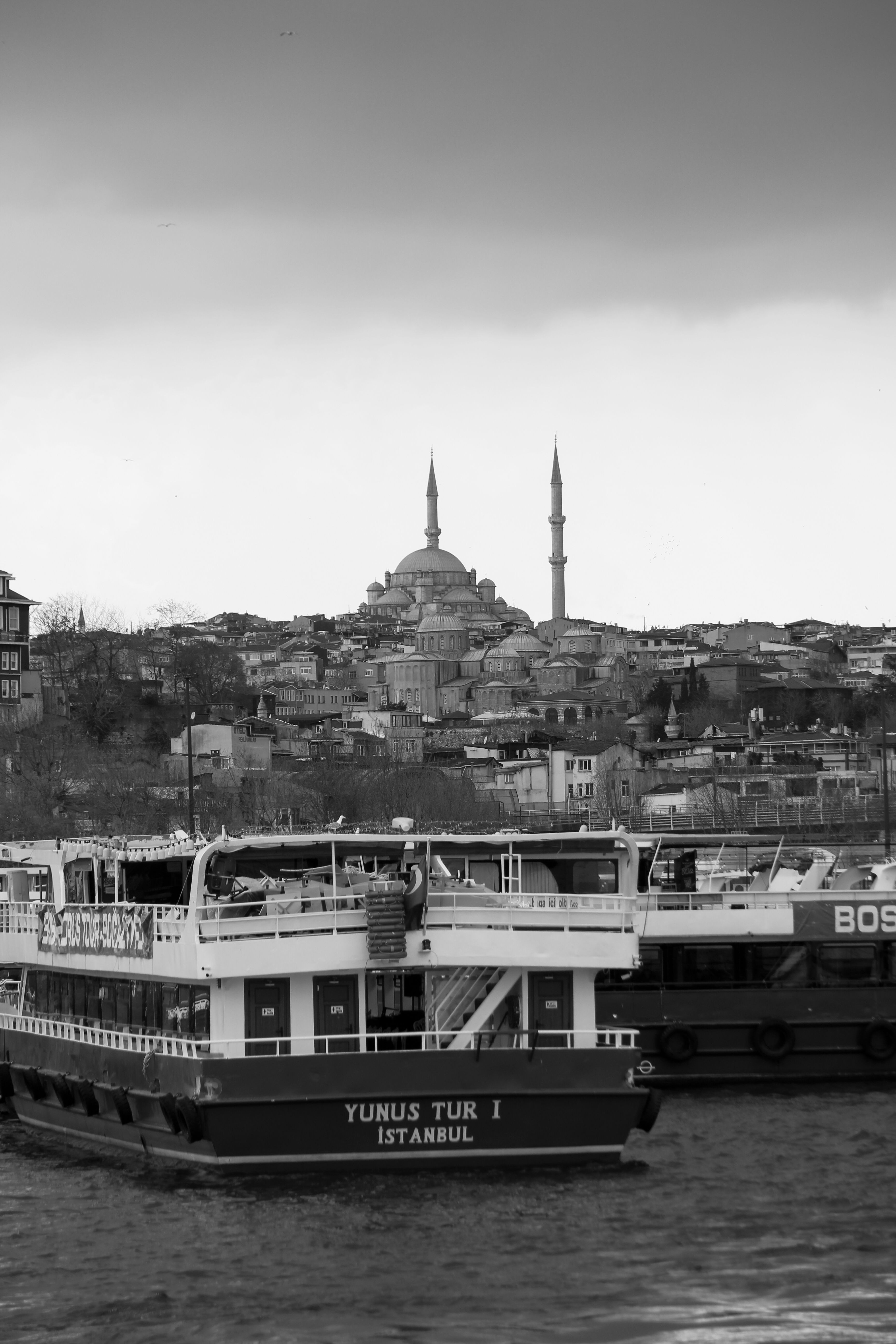 Dramatic black and white photo of Istanbul skyline with boats and historic mosque view.