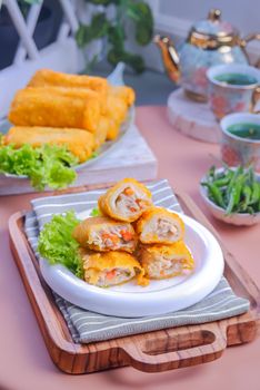 Delicious crispy spring rolls served with green tea and fresh vegetables indoors.