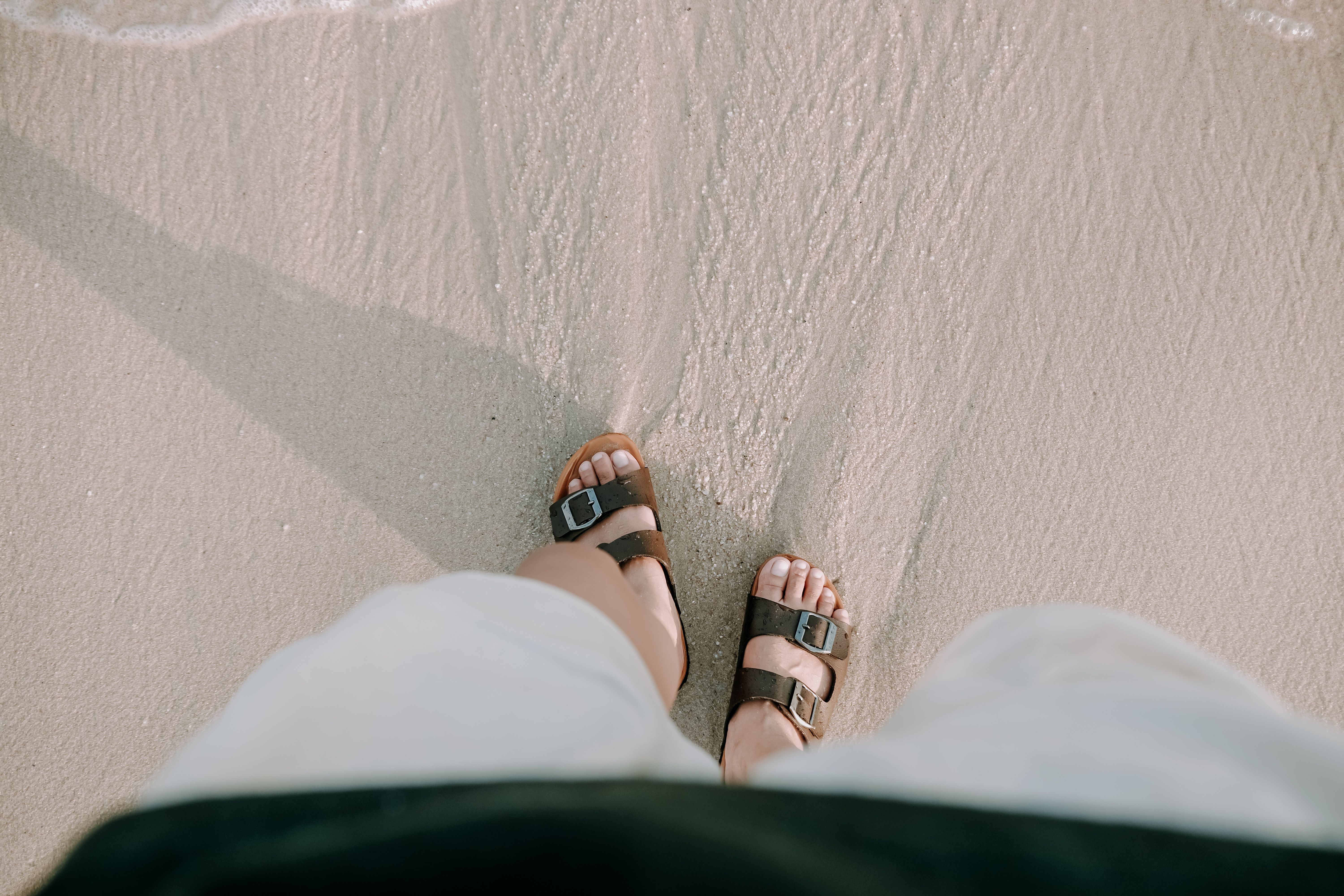 Close-up of feet in sandals strolling on a sandy beach, capturing a serene summer vibe.