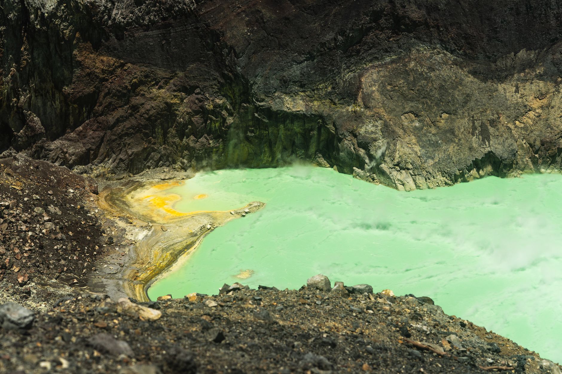 A breathtaking view of a vibrant green sulfuric volcanic crater lake surrounded by rugged terrain.