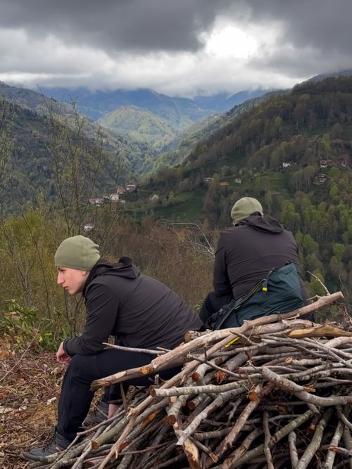 Free Two hikers rest in a scenic mountain setting, surrounded by lush greenery and a dramatic sky. Stock Photo