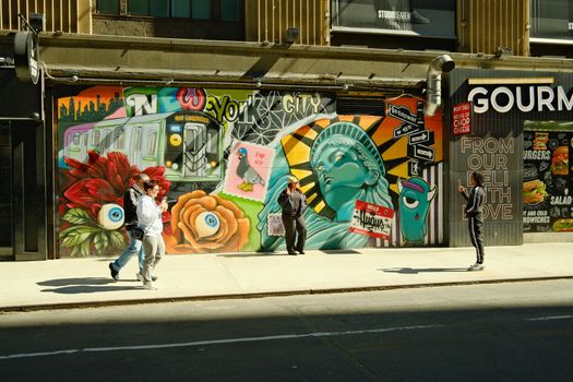 Vivid mural depicting NYC symbols on city street with pedestrians taking photos.