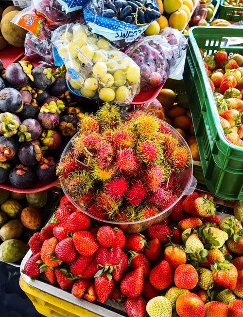 Free A vibrant array of tropical fruits including rambutan, strawberries, and mangosteen at a market stall. Stock Photo