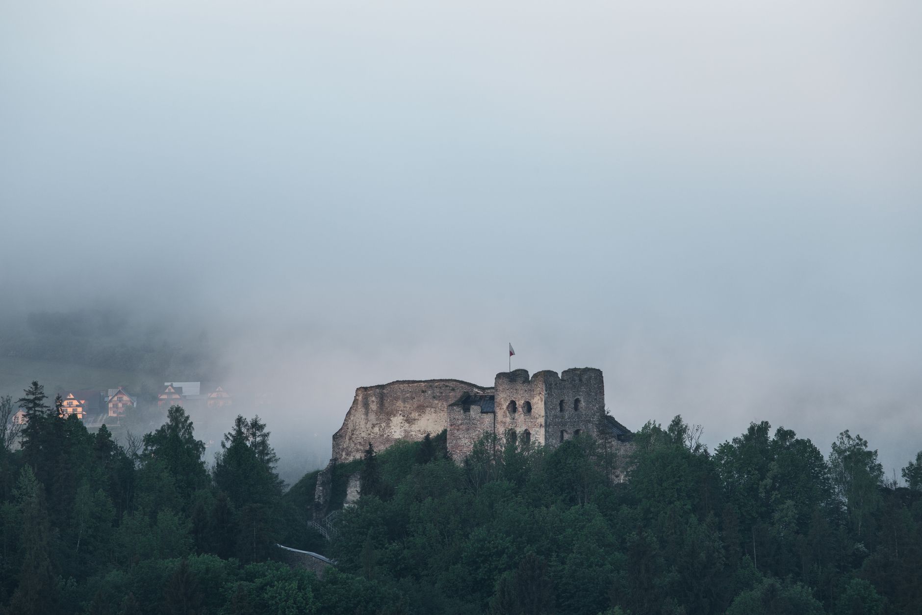Ruined mountain castle walls perched on a limestone ridge above forest