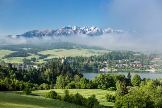 Une vue à couper le souffle sur les montagnes des Tatras enveloppées de brume, avec un paysage verdoyant luxuriant au premier plan.