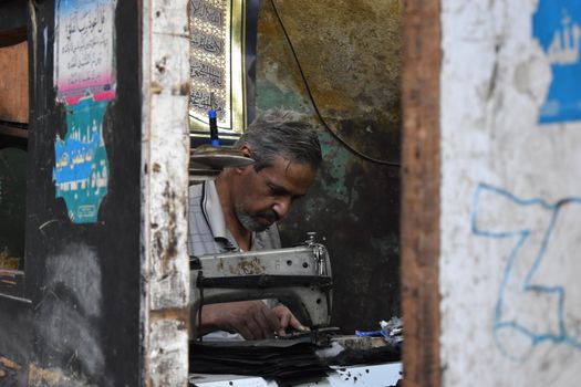A tailor focused on his work at a sewing machine in a rustic shop in Cairo, Egypt.
