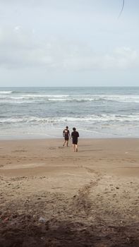 Serene view of two adults walking on a sandy beach by the ocean, under a cloudy sky.