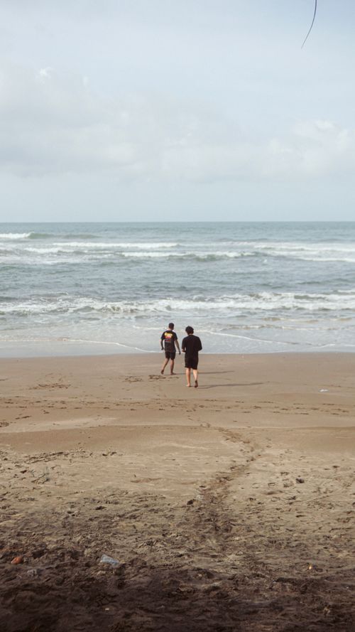 Free Serene view of two adults walking on a sandy beach by the ocean, under a cloudy sky. Stock Photo