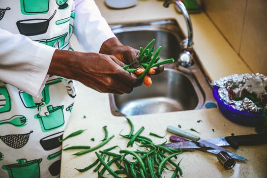 Hands of a chef preparing fresh green beans on a kitchen countertop near a sink.