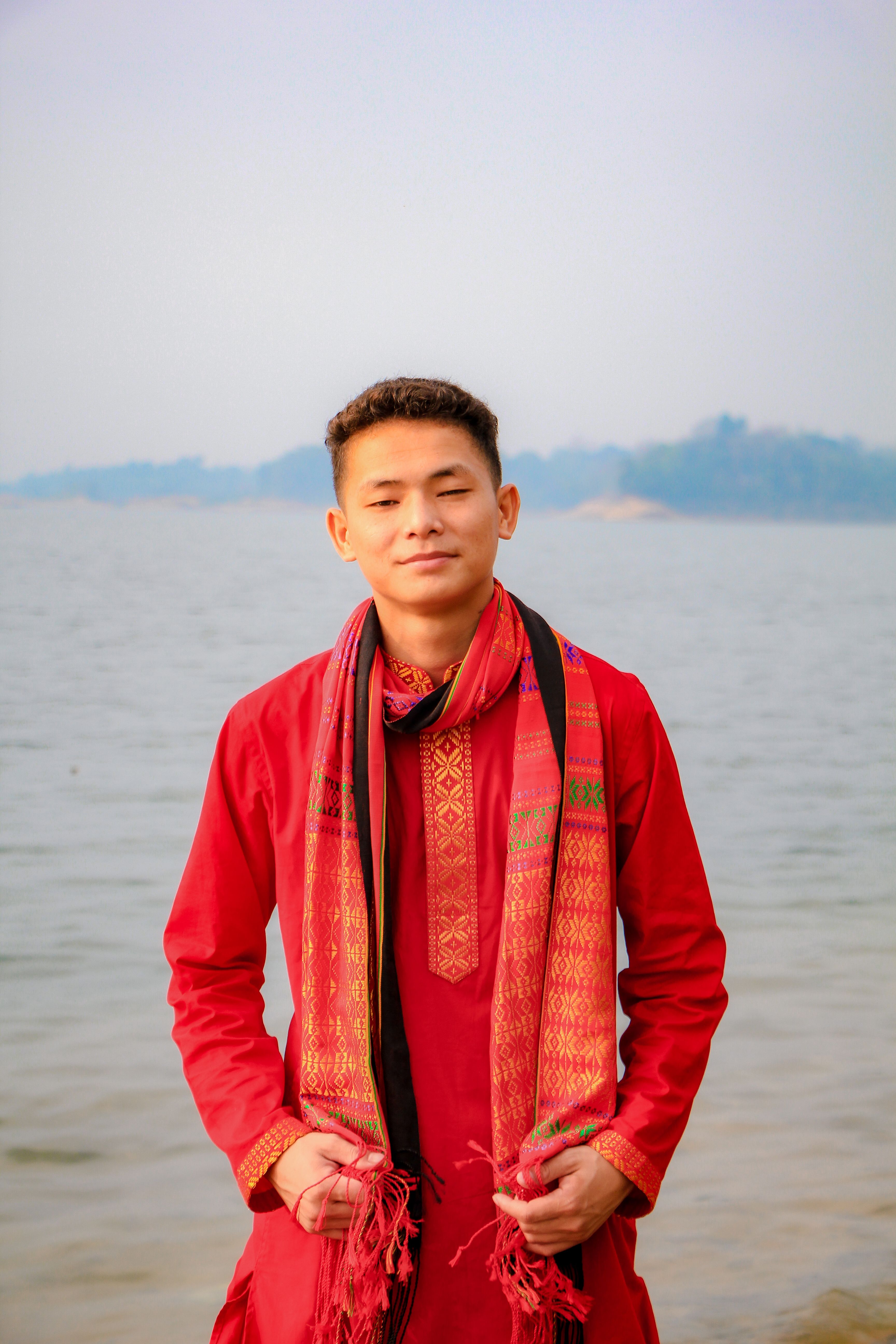 Young man in traditional red attire by the serene Rangamati Lake in Bangladesh.