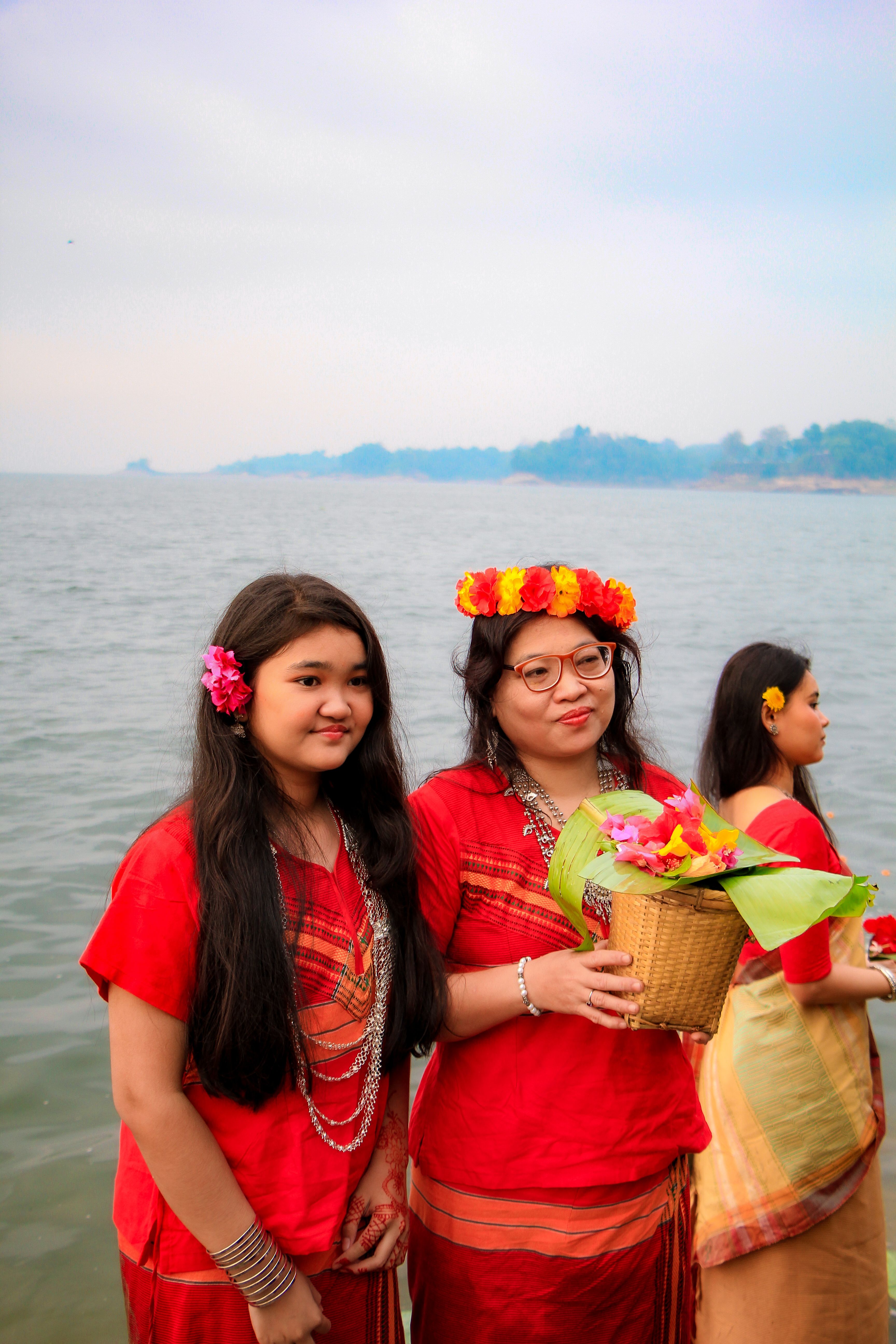 Women celebrating Phool Biju by Rangamati Lake, showcasing vibrant traditional attire and floral offerings.