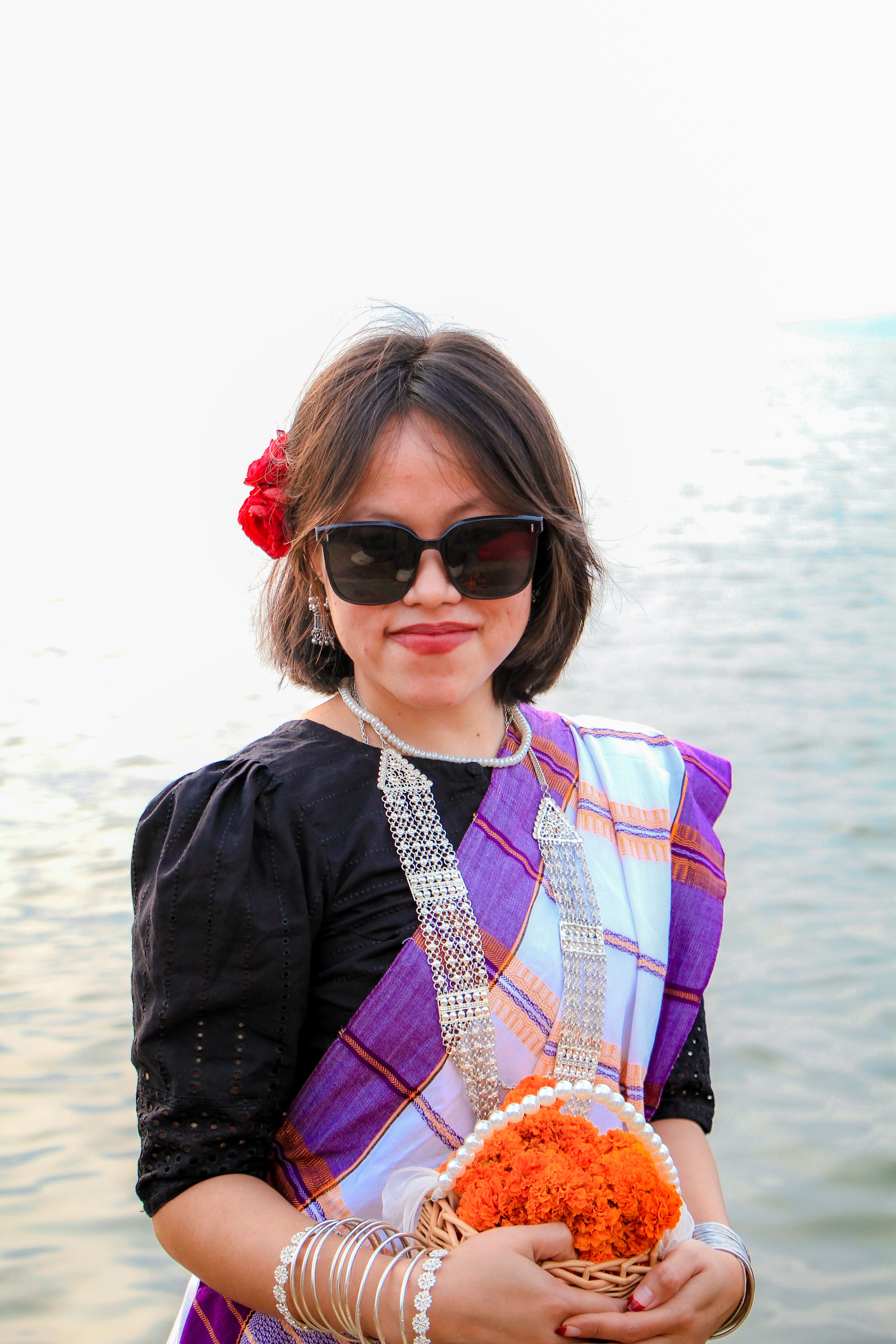Woman in traditional attire holding flowers by a river in Rangamati.
