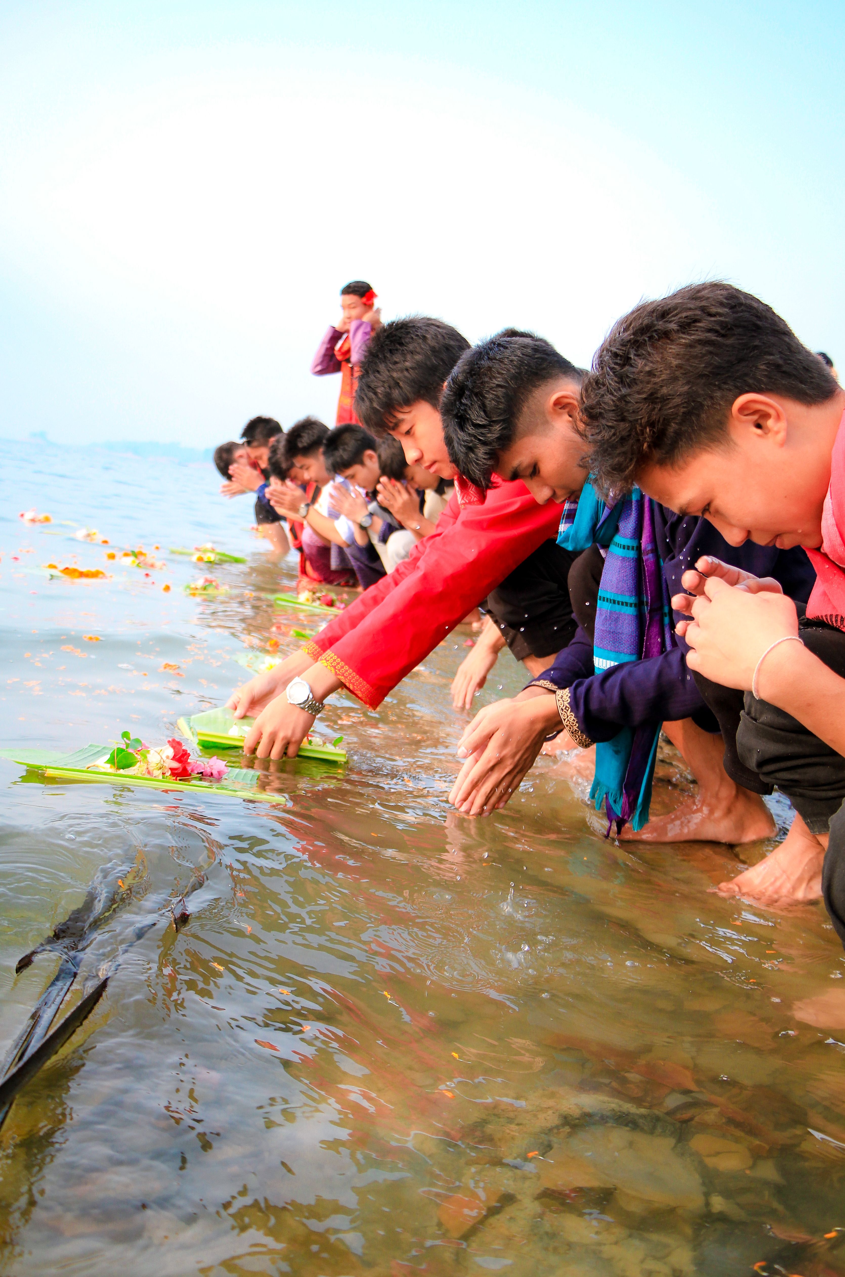 People participating in a cultural flower offering ceremony by the water in Rangamati, Bangladesh.