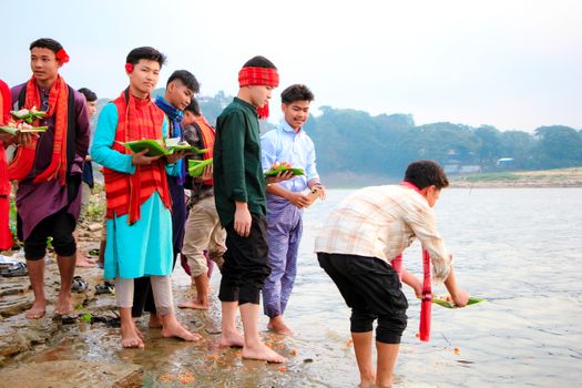 Men participate in a traditional river ritual in Rangamati, Bangladesh, with vibrant attire and floral offerings.