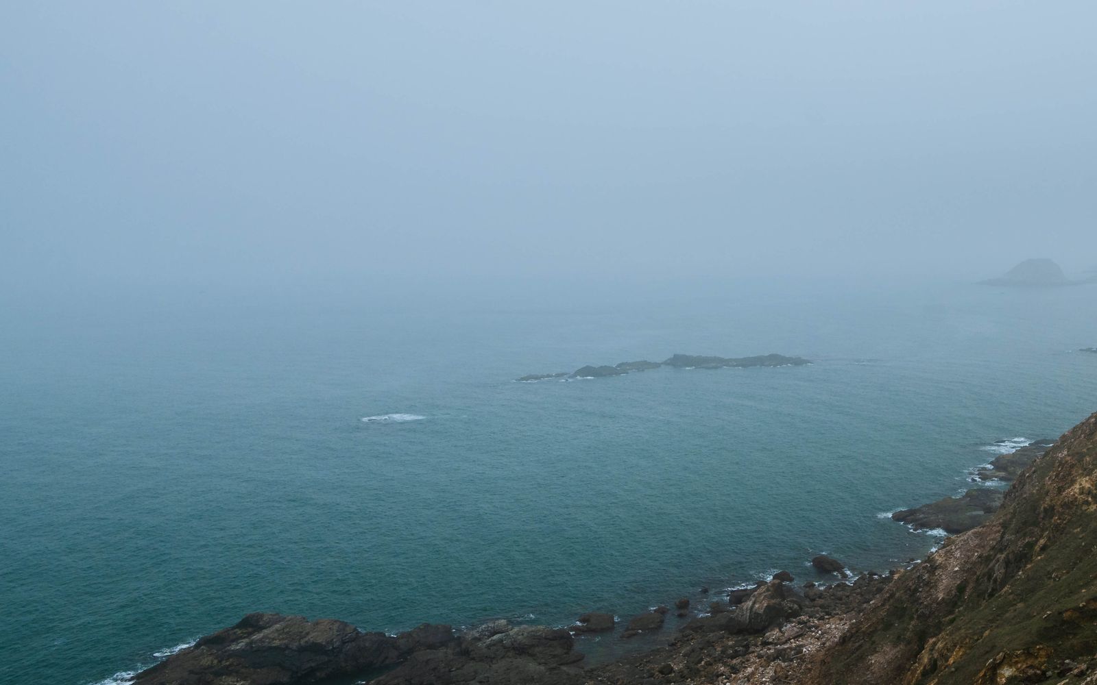 Thick fog over rocky coastal cliffs above the ocean.