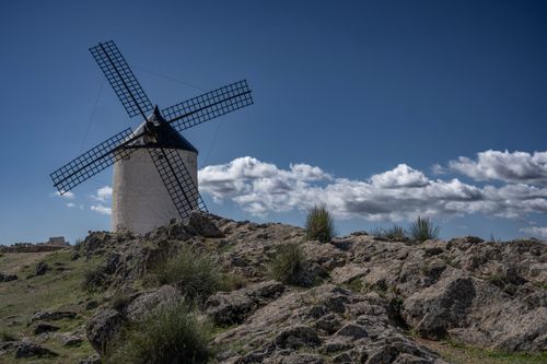 Free Scenic view of a traditional windmill in Consuegra, Spain, with rocky foreground and a bright blue sky. Stock Photo