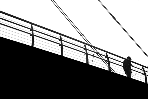 Free Black and white silhouette of a person walking on a cable bridge. Stock Photo