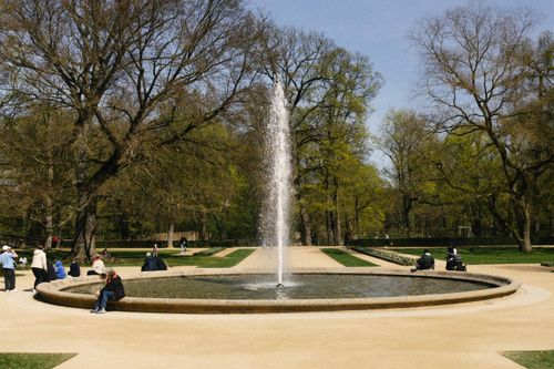 Free A tranquil fountain in a park full of visitors enjoying a sunny spring day. Stock Photo