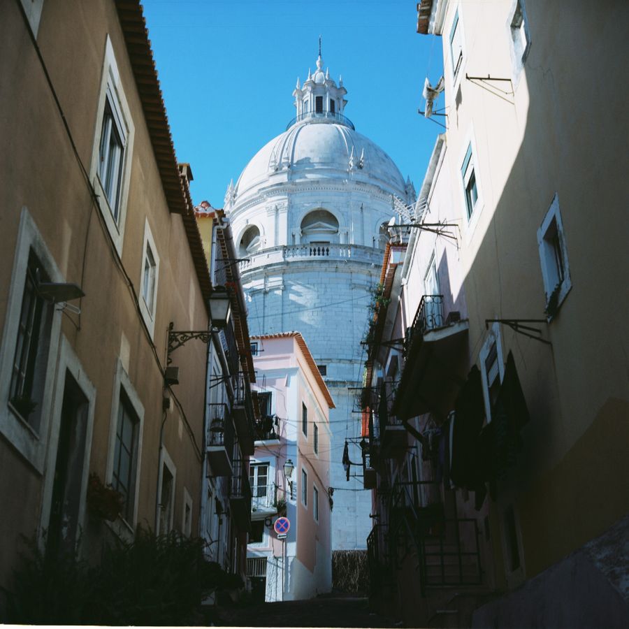 A narrow Alfama street climbing toward a domed church in the morning sun — photo by Efe Ersoy on Pexels