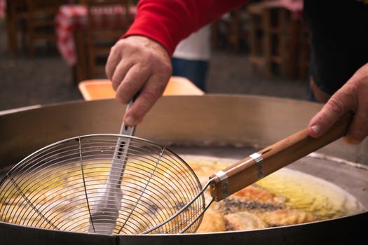 Close-up of a street vendor frying snacks in a large pan with a metal skimmer. Captured outdoors.