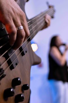 A focus on a musician playing bass with a blurred singer in the background, creating a dynamic concert atmosphere.