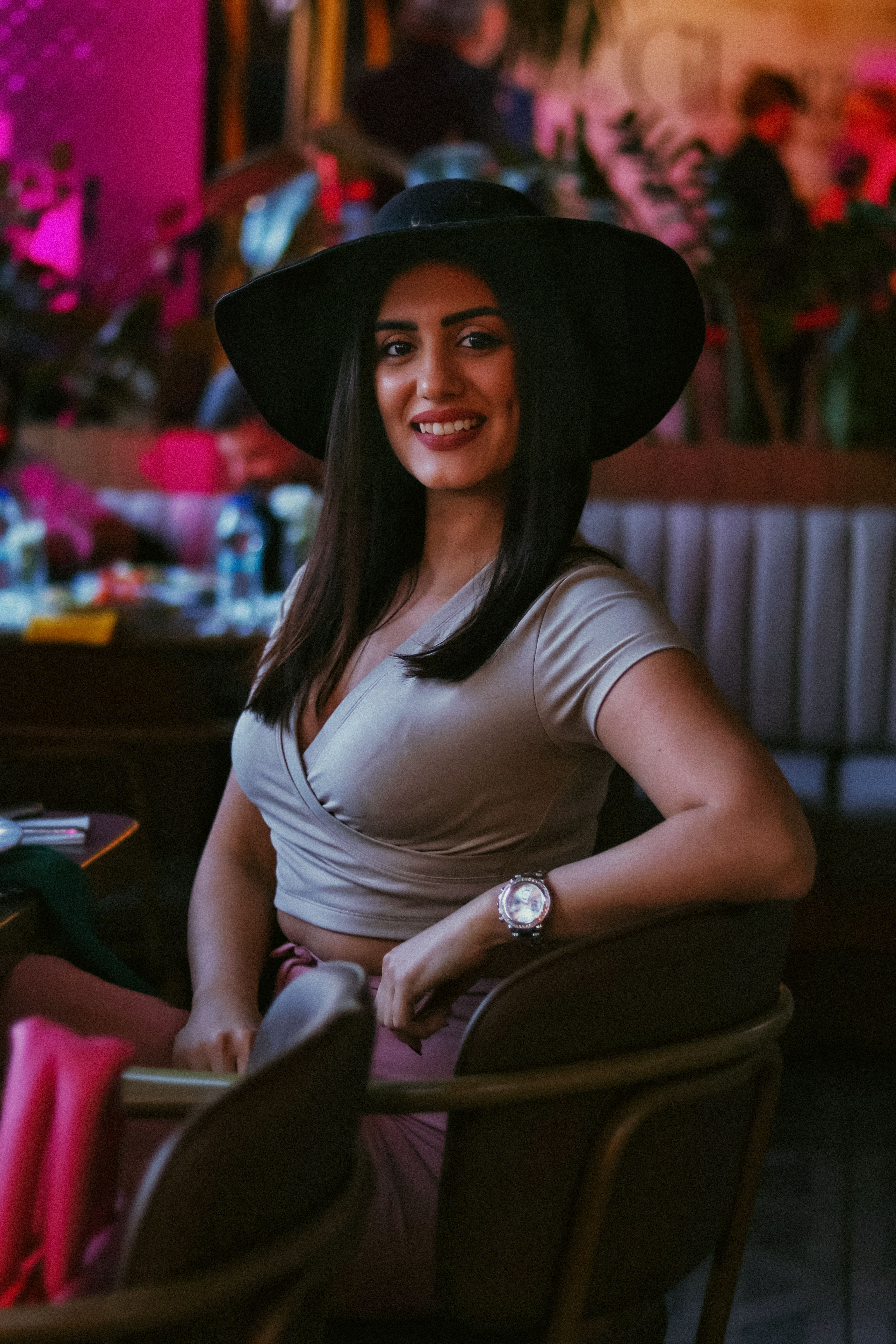 Stylish woman in a hat seated indoors, exuding confidence and charm.