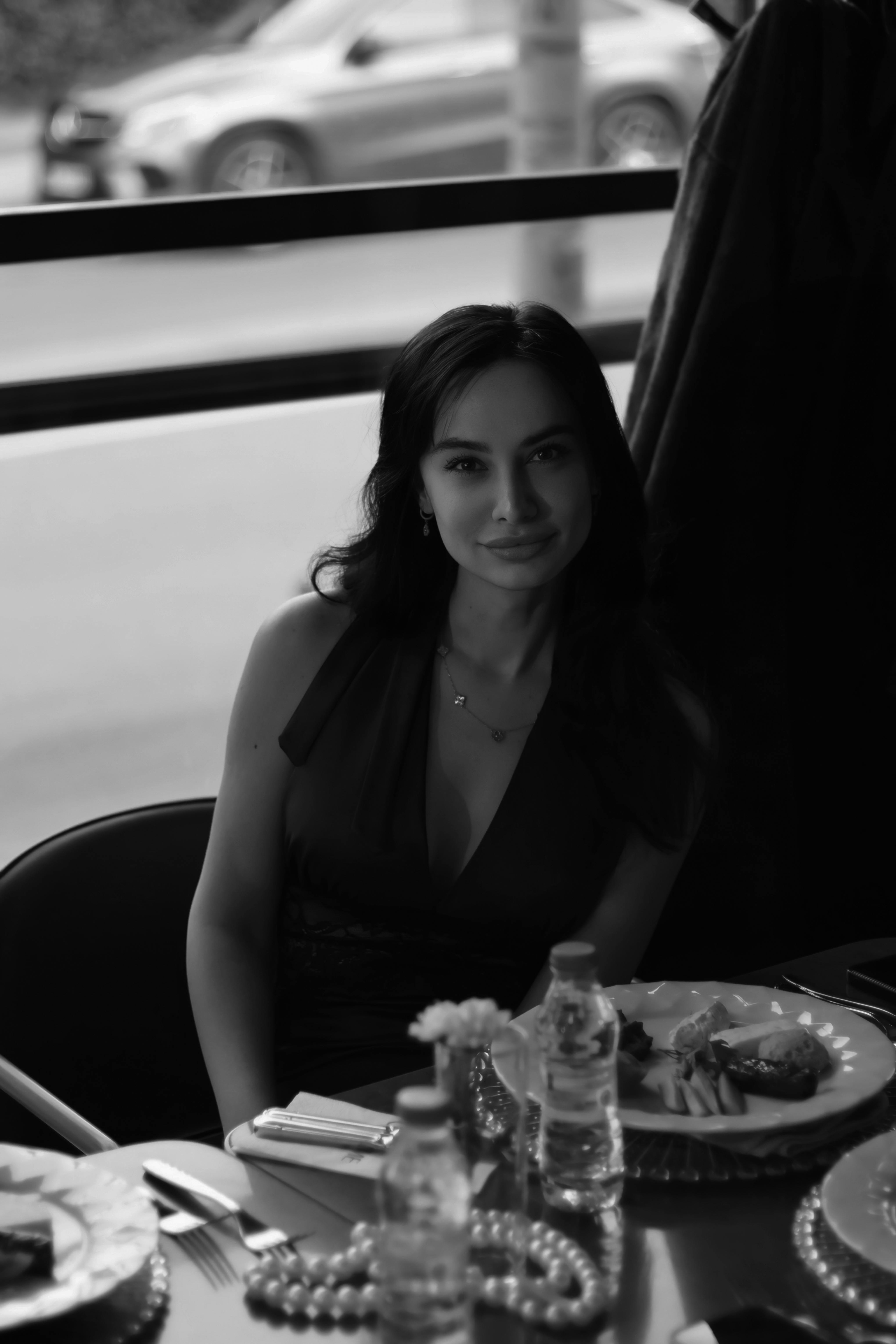 Elegant black and white portrait of a woman seated at a dining table.