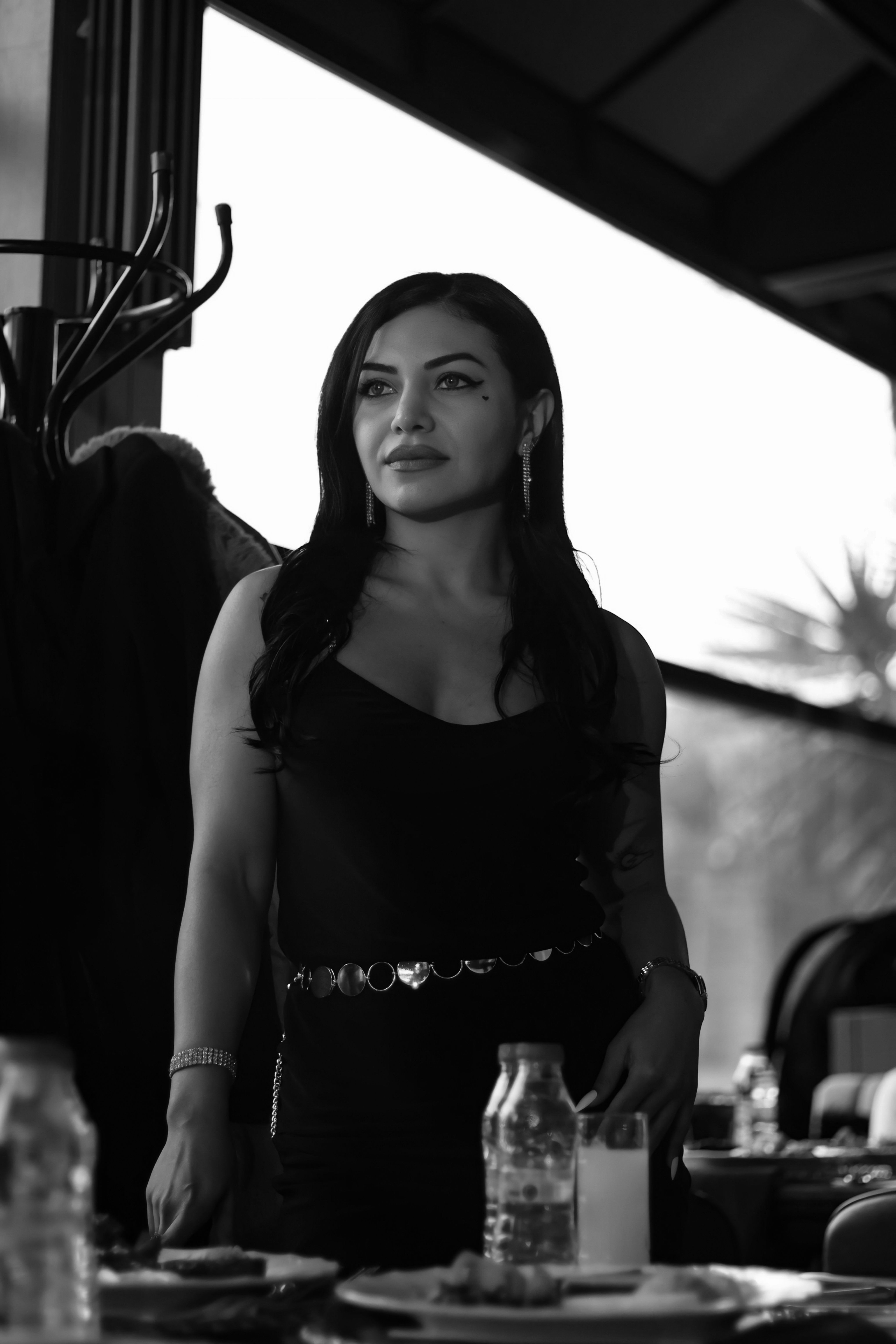 Elegant woman standing indoors, captured in a moody black and white portrait.