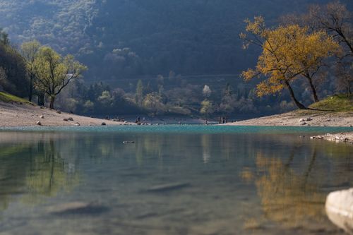 Free Calm lake scene with autumn trees and distant people in Italy's serene landscape. Stock Photo