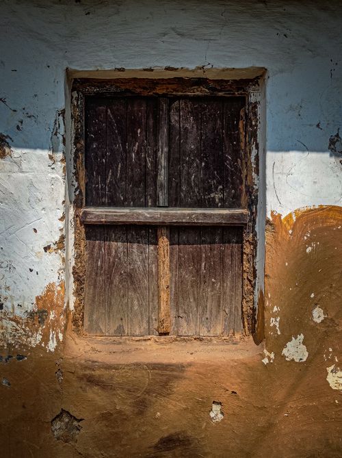 Free A rustic wooden window set in an aged, textured wall with peeling plaster and earthy tones. Stock Photo