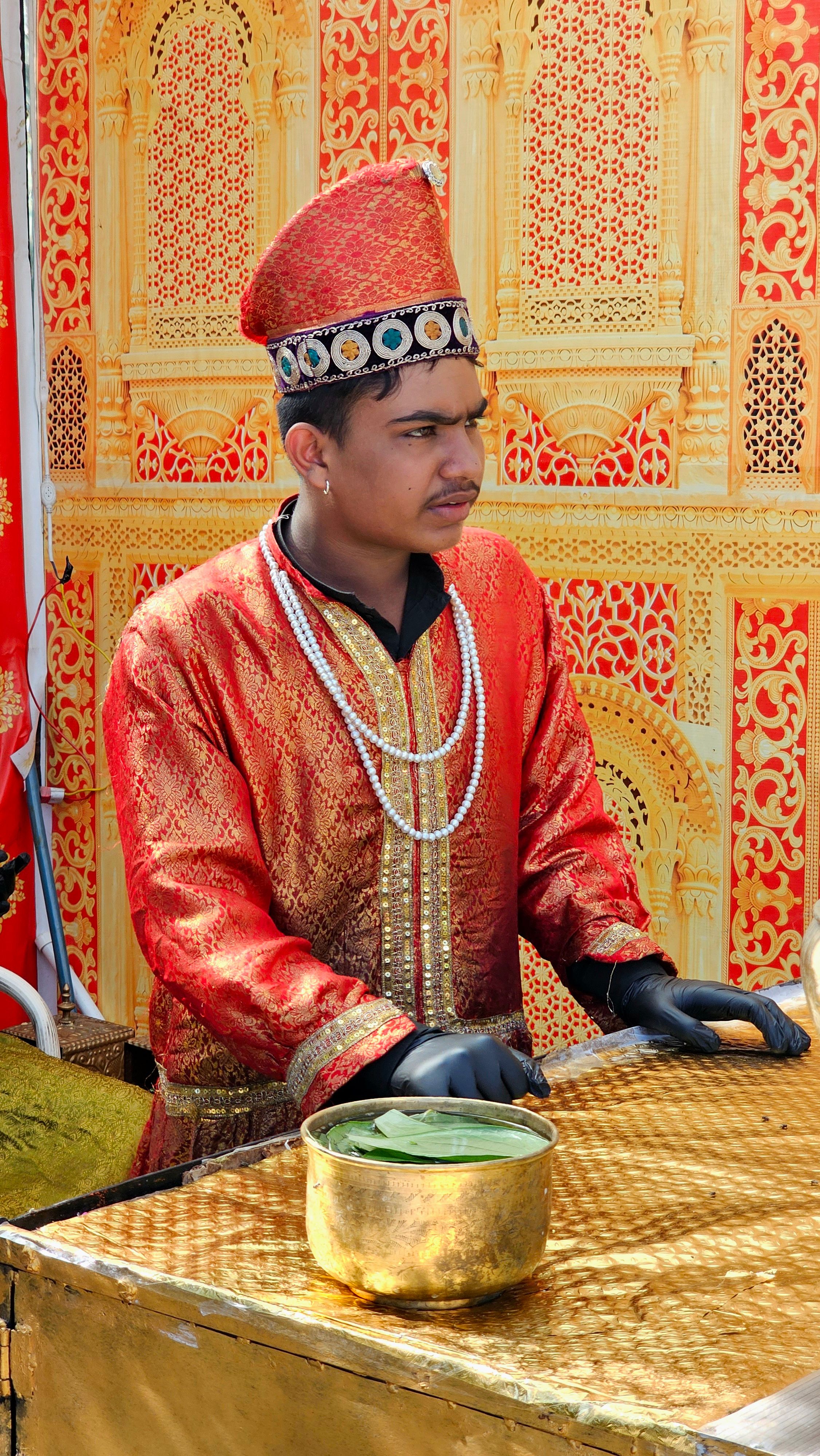 A traditionally dressed Indian vendor preparing paan leaves at a cultural event.