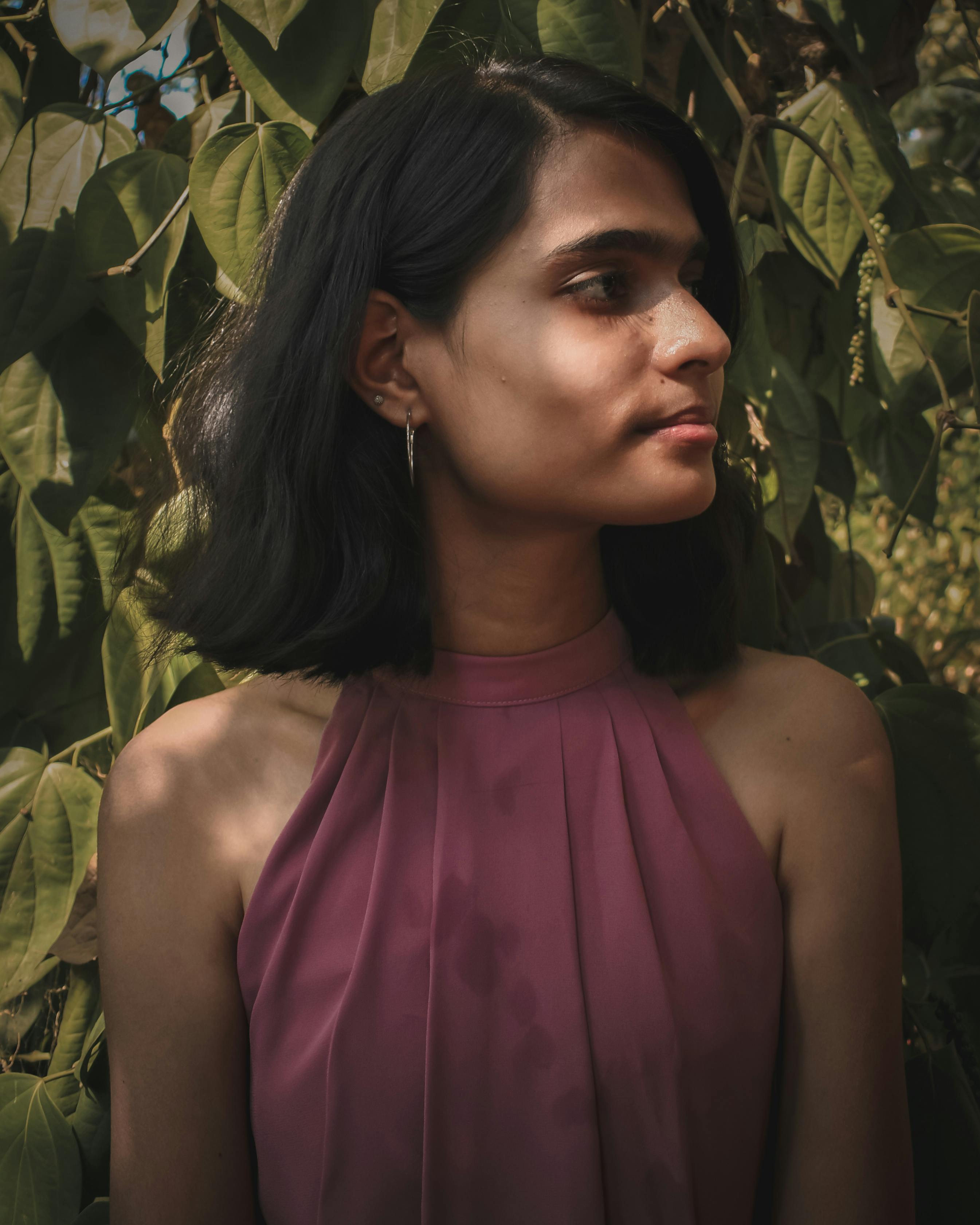 Portrait of a woman in a mauve dress surrounded by green leaves, exuding a serene and thoughtful mood.