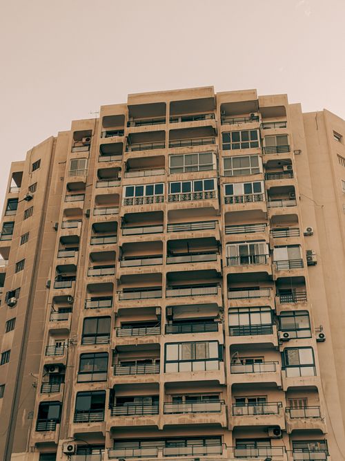 Free A towering beige high-rise apartment building under a clear sky, with various balcony and window styles. Stock Photo