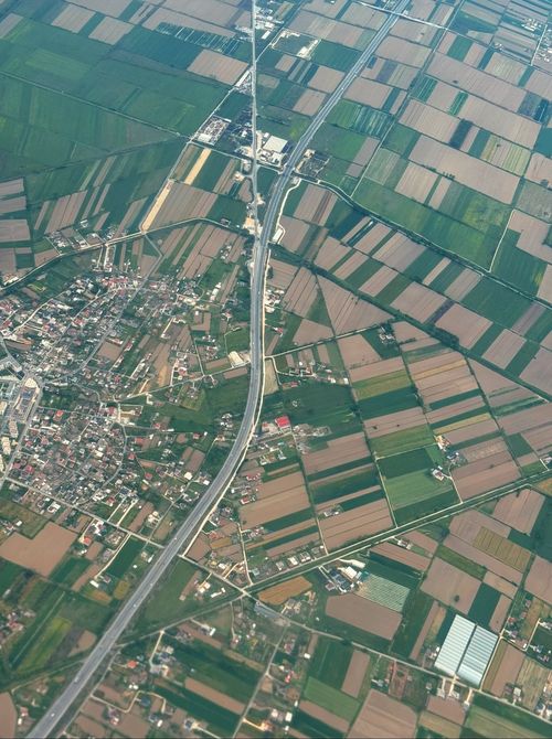 Free Aerial shot capturing the patchwork pattern of farmland intersected by a central road. Stock Photo