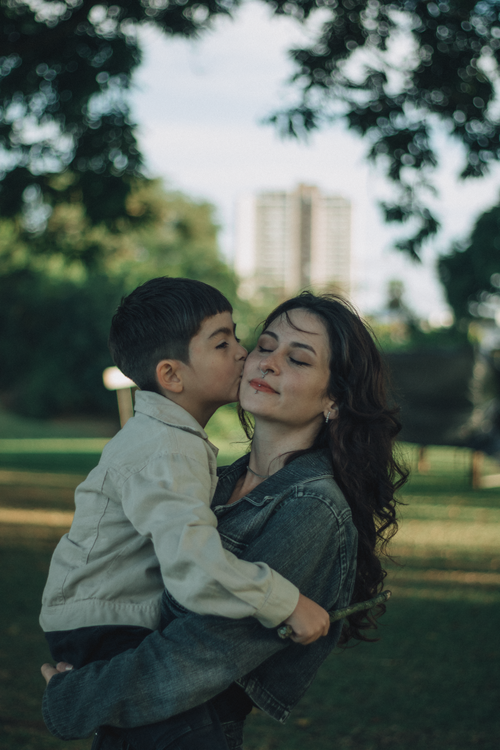 Free A mother and son share a loving embrace and a kiss outdoors in a scenic park setting. Stock Photo