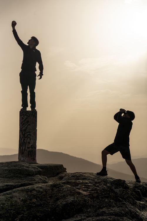 Free Two silhouetted figures on a rocky mountain at sunset, capturing photos. Stock Photo