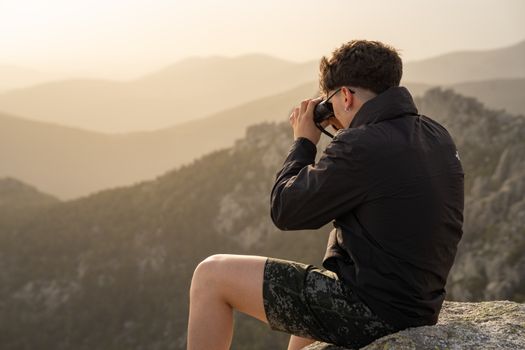 Young man photographing mountain landscape during sunset with camera.
