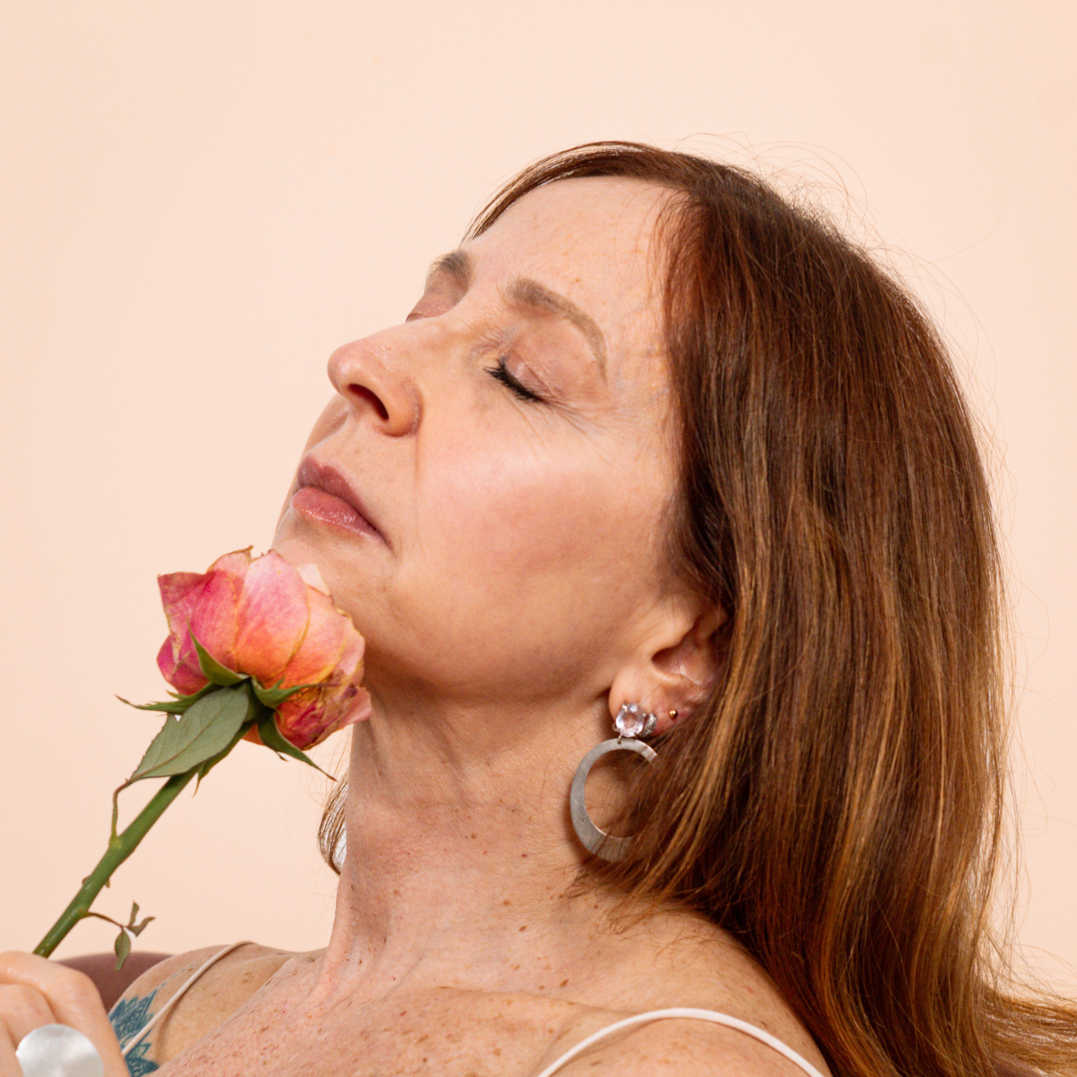 Close-up portrait of an adult woman gently holding a pink rose, exuding elegance and serenity.