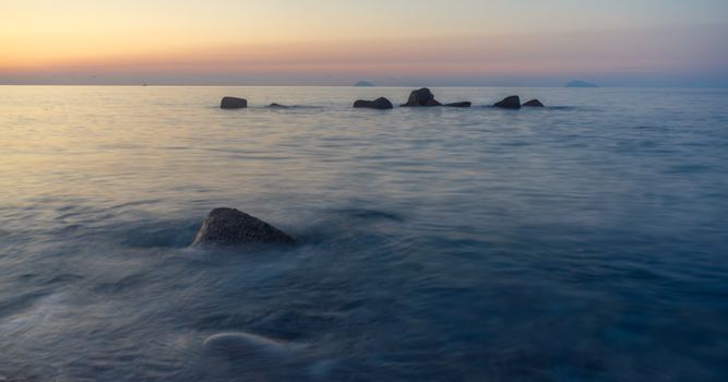 A tranquil ocean scene at sunset with rocks emerging from calm waters.