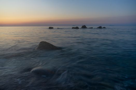 Peaceful sunset view over the ocean with distant rocks and calm waters, perfect for a serene landscape.