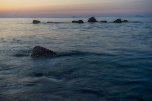 Peaceful ocean view at sunset with rocks and tranquil waters creating a serene atmosphere.