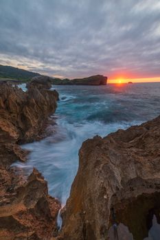 Beautiful sunset over a rocky coastline with vibrant sky and waves crashing.