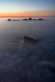 Serene view of the ocean at sunset with calm waters and rocks in silhouette.