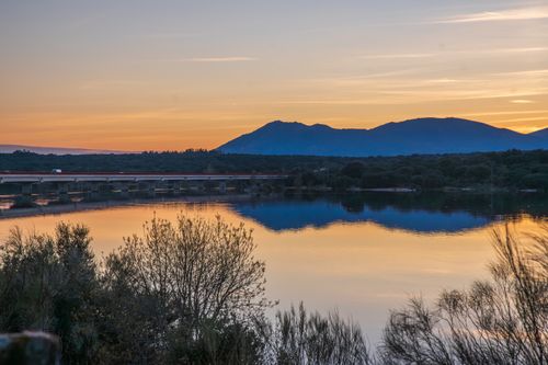 Free A tranquil sunset view over a lake with mountains and a bridge reflecting on the water. Stock Photo