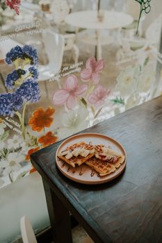 Plate of waffles drizzled with syrup on a wooden table in a beautifully decorated floral cafe.