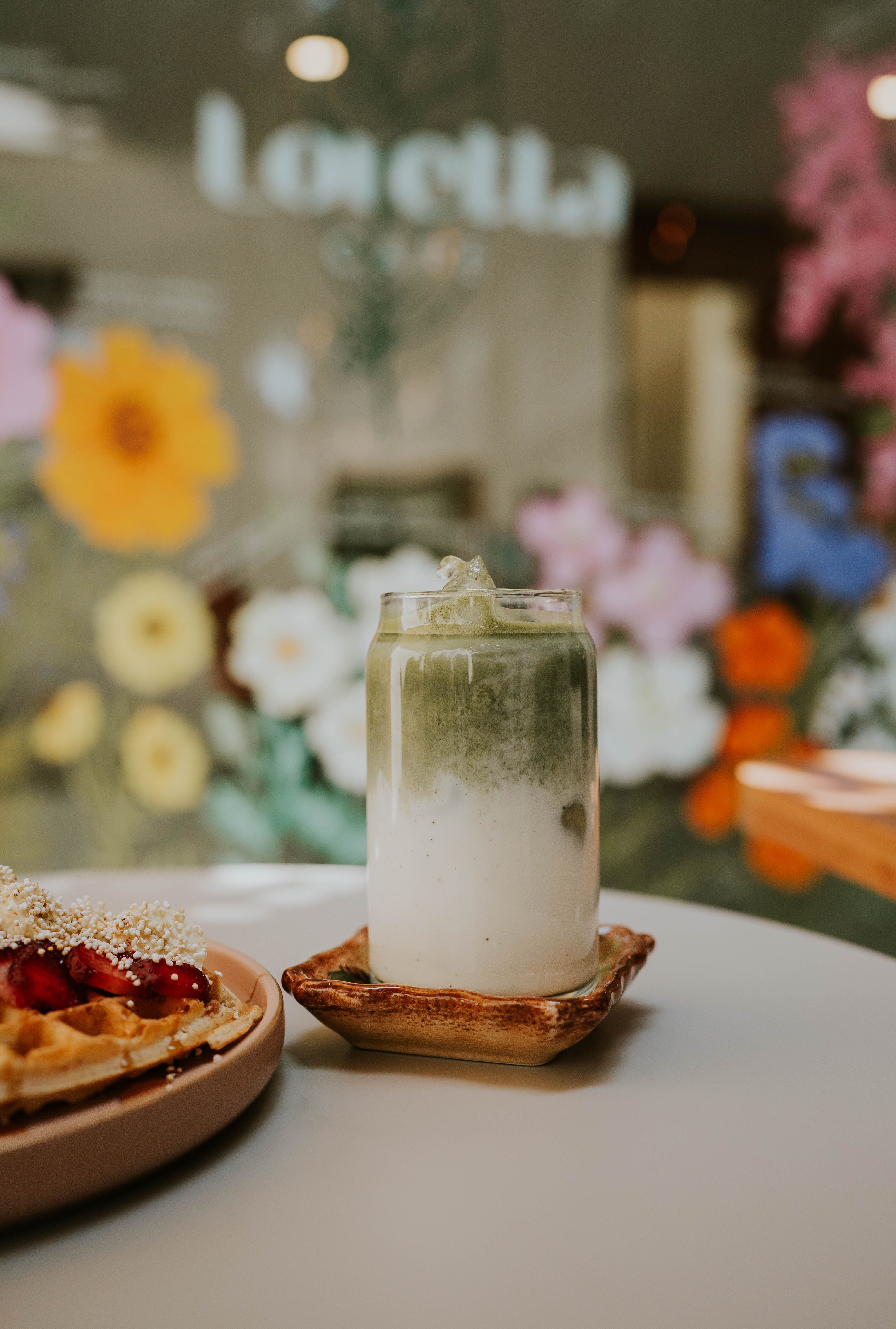 A cozy table setting with a matcha latte and waffle in a floral-decorated cafe.
